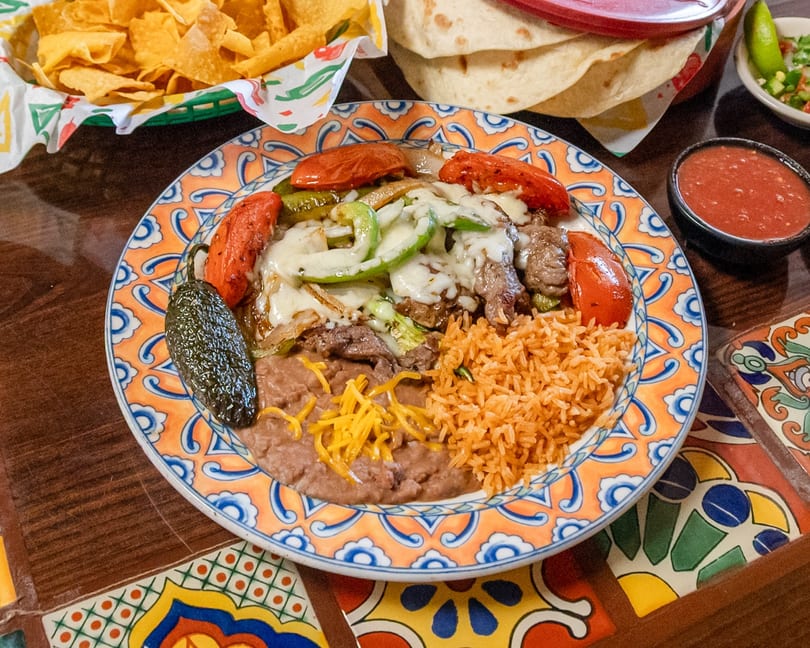 Mexican fajita plate with steak, melted cheese, bell peppers, rice, refried beans, and a grilled jalapeño.