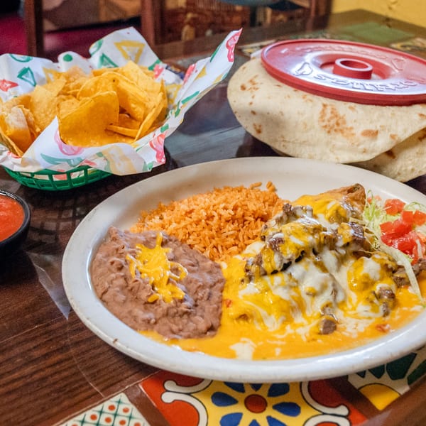 Platter of cheesy Mexican entree with rice, refried beans, chips, salsa, and warm tortillas.