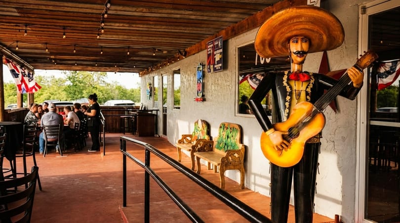 Outdoor patio of a Mexican restaurant with a mariachi statue, diners, and festive decor.