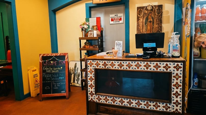 A vibrant Mexican restaurant interior with a tiled counter, chalkboard sign, and colorful decor.