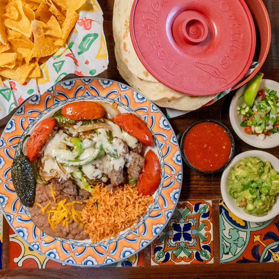 Colorful Mexican food spread with fajitas, rice, beans, chips, tortillas, salsa, guacamole, and pico de gallo.